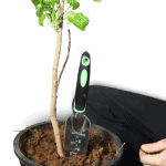 Garden hand trowel in soil next to a potted plant for gardening.